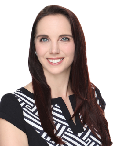 A woman with long brown hair, wearing a black and white patterned top, smiles at the camera against a white background.