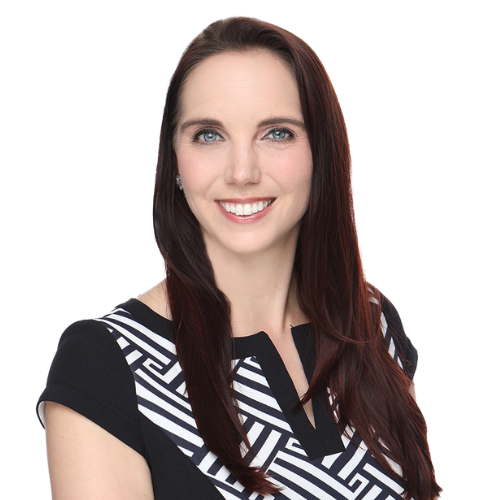 A woman with long brown hair, wearing a black and white patterned top, smiles at the camera against a white background.