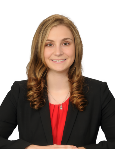 A woman with long wavy hair wearing a black blazer and red top is smiling and seated at a table.