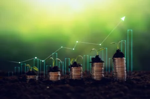 Stacks of coins with seedlings growing on top are arranged in increasing order, against a background of a bar graph and arrow indicating economic growth.